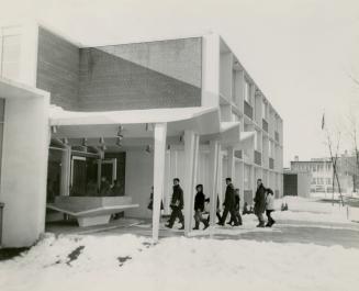 Picture of boys and girls entering the door of a school in winter with snow on the ground. 