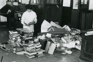 Picture of library staff member looking through a pile of books on the floor damaged by fire. 