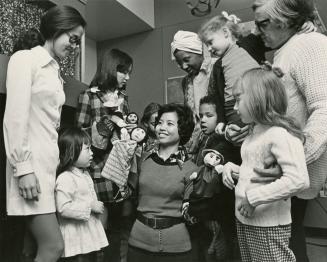 Picture of a librarian with puppets surrounded by children and adults. 