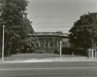 Picture of a one storey library building covered in vine and with trees on both sides and phone…