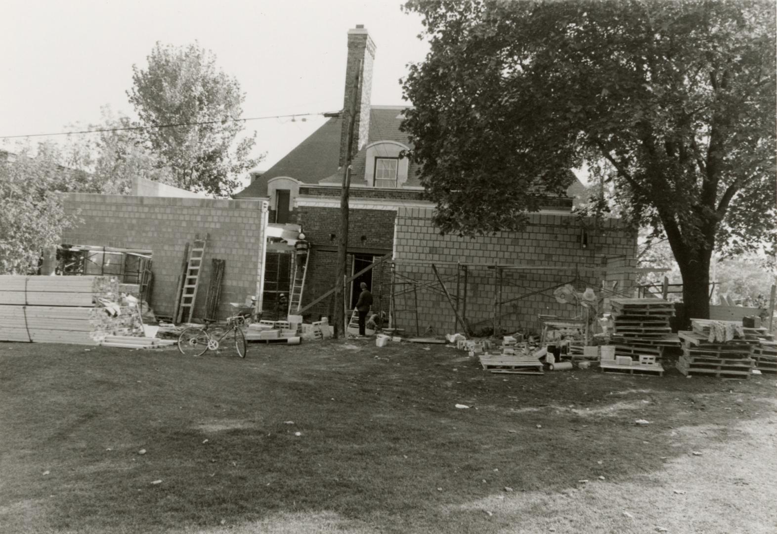 Picture of construction of brick library building with lawn in foreground and large tree on rig…