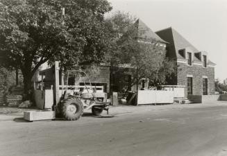Picture of side view of library with street, large tree, construction vehicle and original 1930…