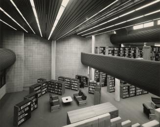Picture of interior of modern library looking down from an upper level at shelving and tables w…