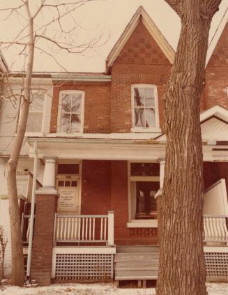 Picture of a Victorian row house with porch and tree trunk in front. 