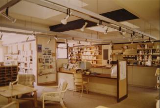 Picture of library interior showing people browsing shelves of books and table and two chairs i…