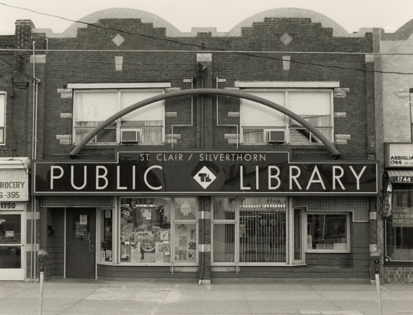 Picture of exterior of two storey library building in storefront with large sign above two form…