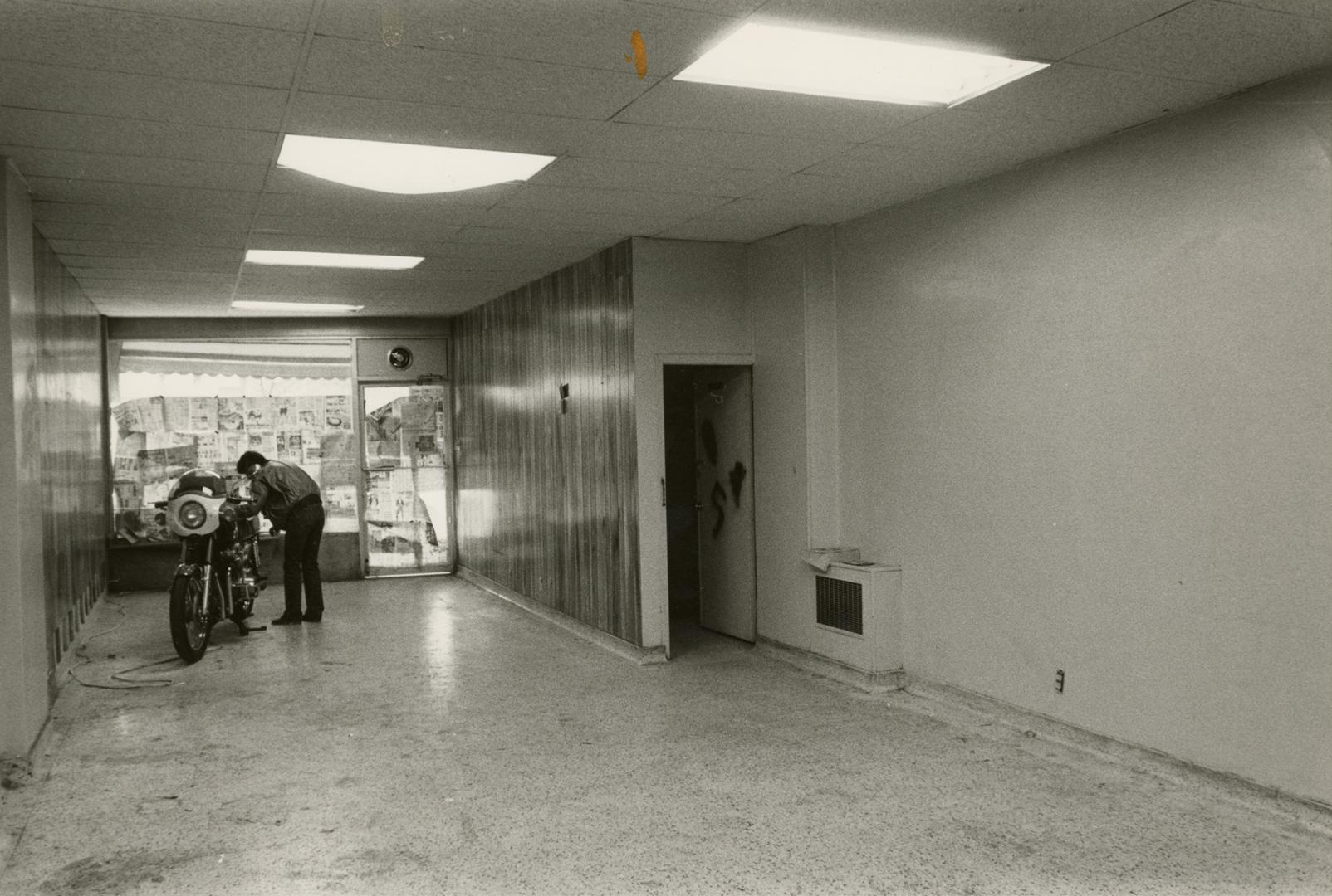 Picture of interior of empty store showing a window and man with motorbike inside the room. 