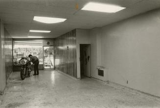 Picture of interior of empty store showing a window and man with motorbike inside the room. 