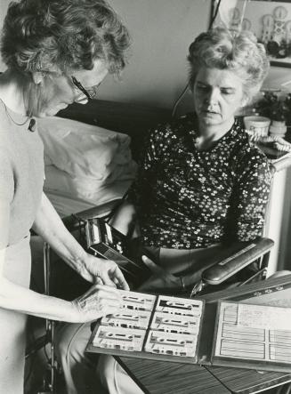 Picture of a librarian selecting a cassette tape from a box for a woman in a wheelchair. 