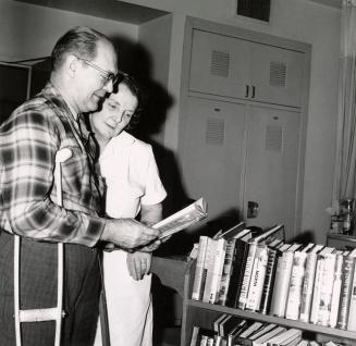 Picture of a woman and man with crutches looking at a book from a library book truck. 