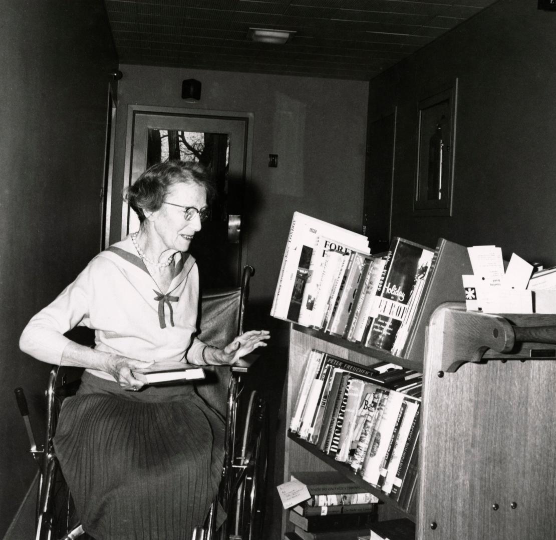 Picture of an older woman in a wheelchair looking at a truck of books. 