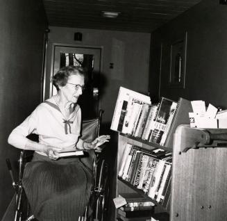Picture of an older woman in a wheelchair looking at a truck of books. 