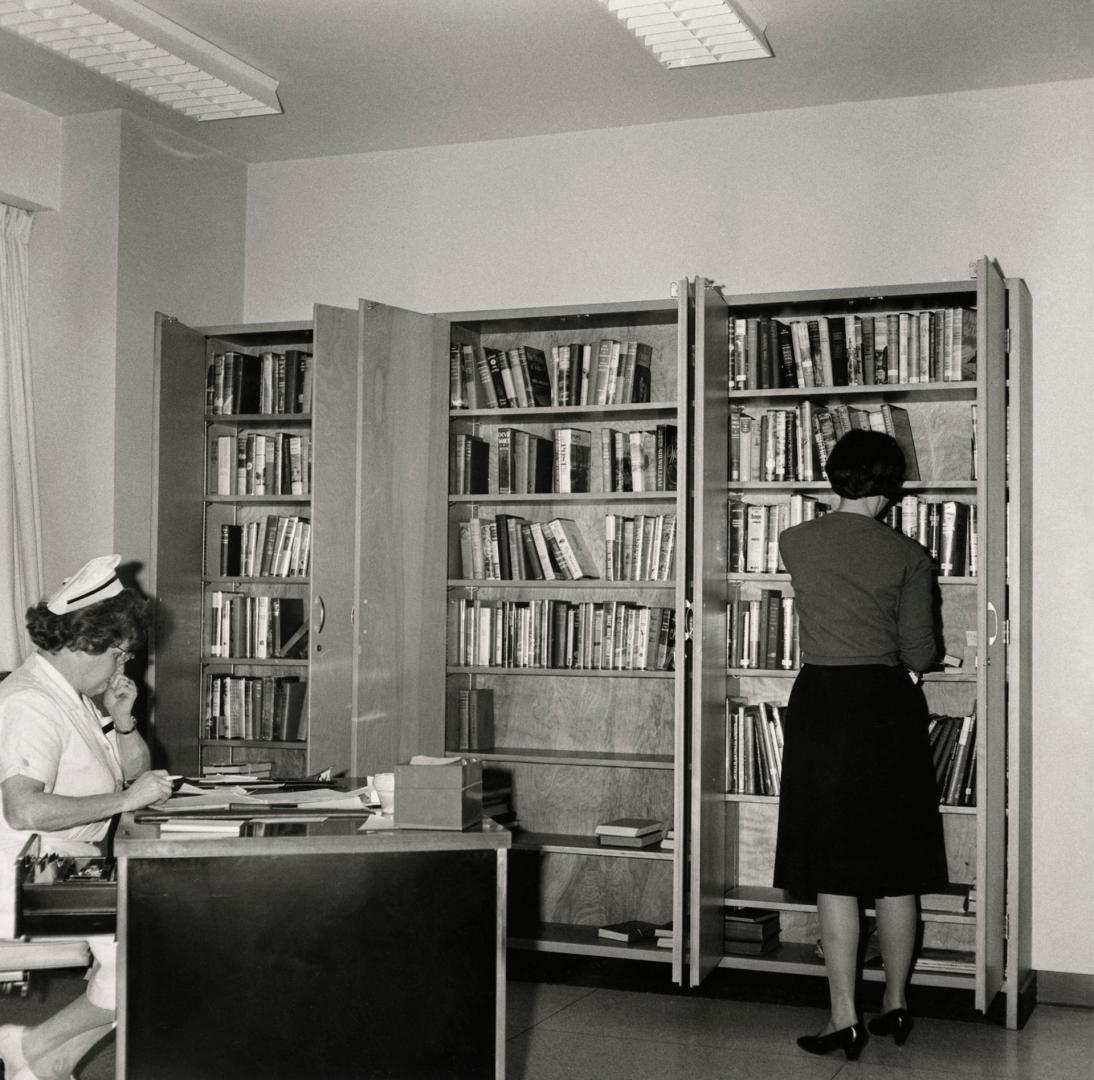 Picture of a librarian looking at book shelves while a nurse sits at a desk. 