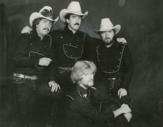 4 young men in a circle on a dark background wearing the same black western shirt. The 3 in bac…