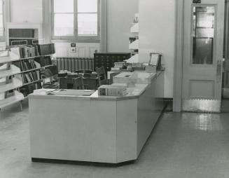 Picture from the side of a 1960 library desk with shelves behind and one large window.