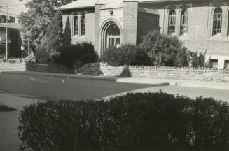 Picture of one storey brick library building with stained glass windows and road and bushes in …