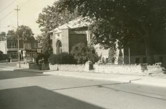 Picture of street and one storey brick library building with trees around it. 