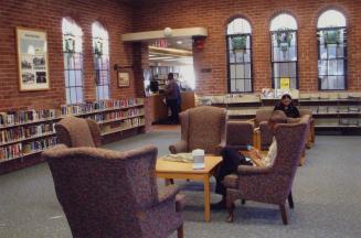 Picture of a room in a library with arched stain glass windows and group of high back chairs an…