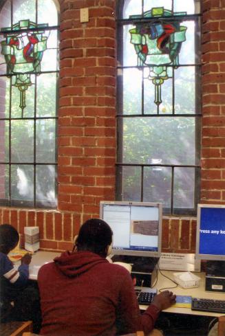 Picture of two stained glass windows in a brick wall and a man on a computer in front. 