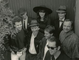 From above: a group of 7 young men and a young woman wearing hats sunglasses and suit jackets. 