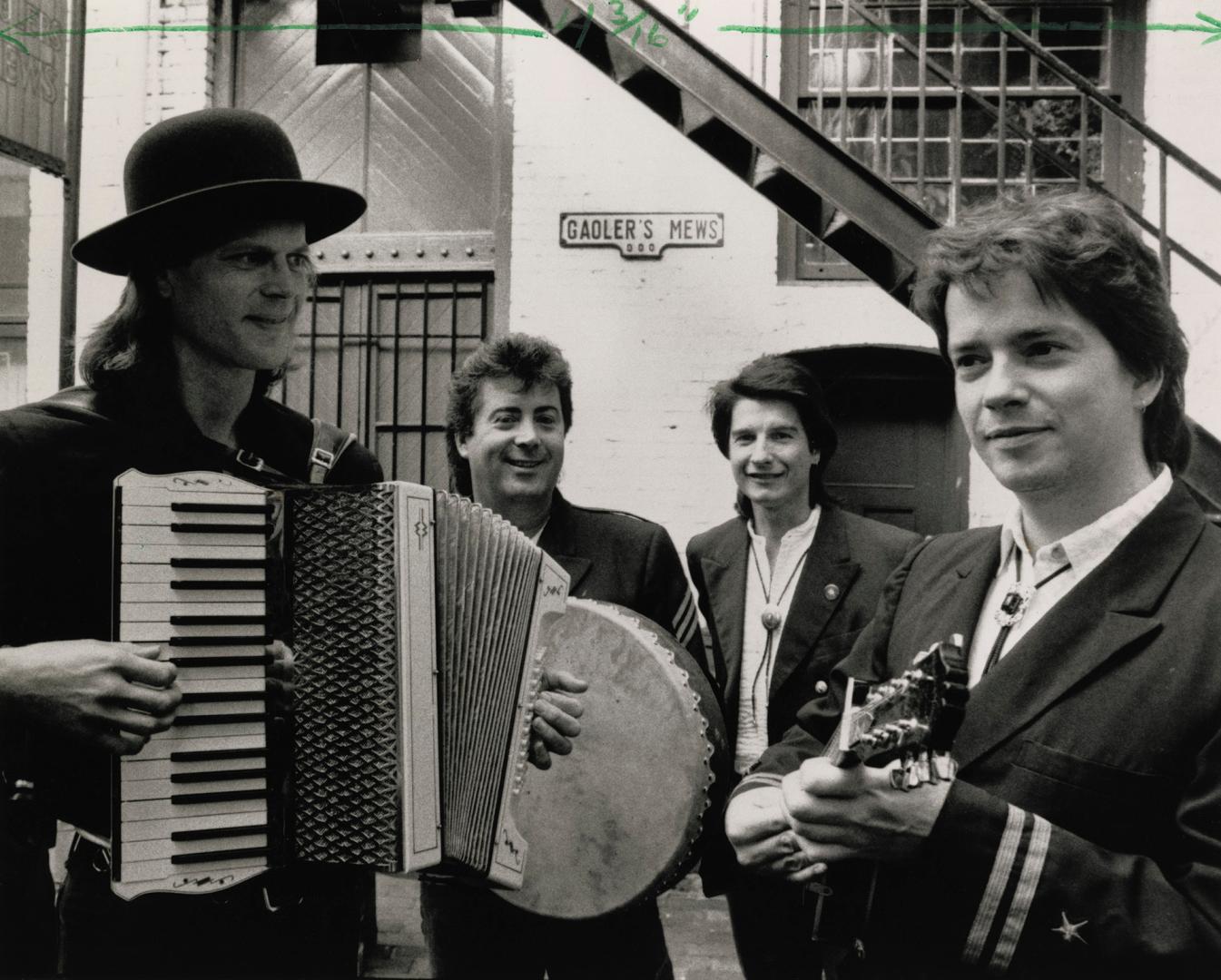 4 men in suits and white shirts in alleyway with sign behind them, Gadler's Mews. From left wit…
