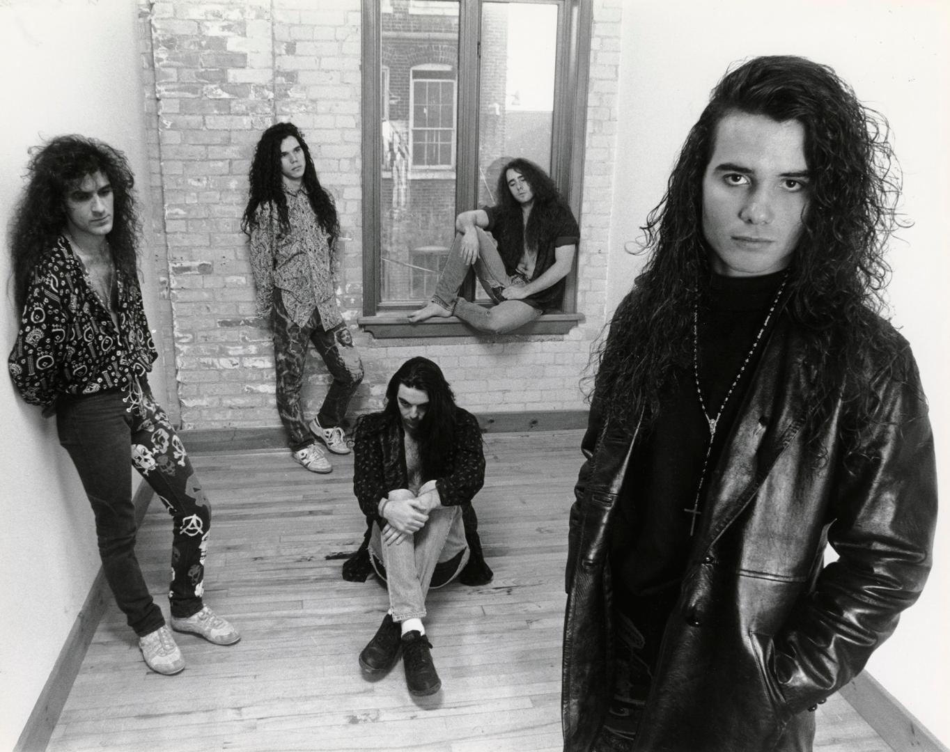 5 young men with long curly hair in jeans and black leather jackets lounge around a small bare …