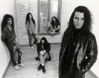 5 young men with long curly hair in jeans and black leather jackets lounge around a small bare …