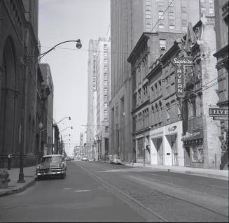 Photograph of street with retail buildings with awnings on right side. 
