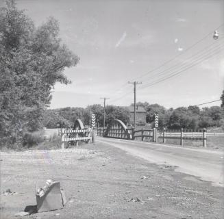 Photography of dirt road and bridge with curved wood sides and trees in background. 