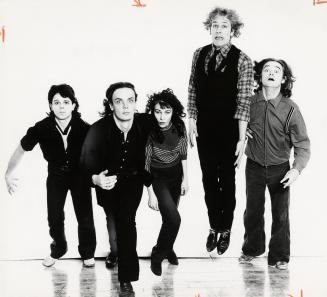 Four young men and a young woman wearing dark clothes against a white background/ They are jump…