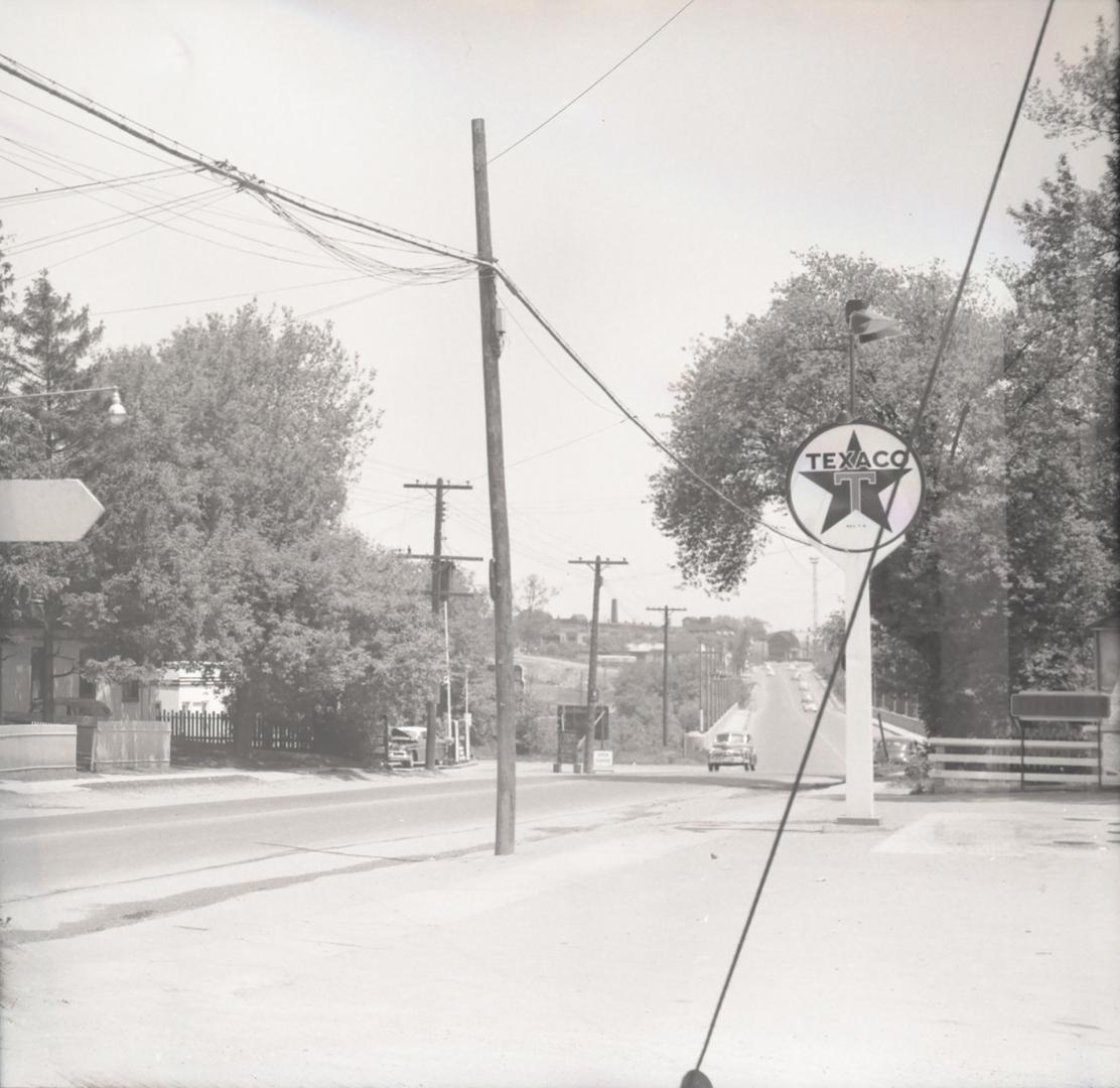 Photograph of street with Texaco sign on rights and trees and telephone poles. 