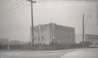 Photograph of street corner and three storey hydro building surrounded by a low hedge. 