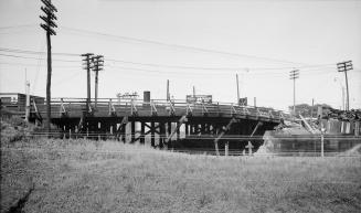 Photograph of road bridge over a gully with several hydro poles in picture. 