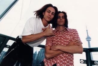 Twins, young men with dark shoulder length hair, tall and slender. CN Tower in background. 