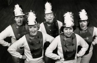 From above, 5 women in majorette jackets and hate with big feathers on the front. 