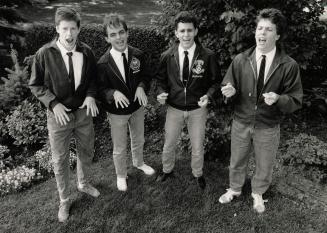 Four young men in a garden singing. They wear chinos, windbreakers, white shirts and ties. 