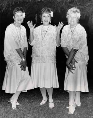 three women in flapper white dresses with white beading on bodices. 