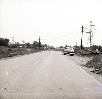 Photograph of empty street with one car parked on right and some hydro lines. 