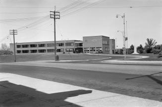 Photograph of a sidewalk and street in foreground and two storey brick municipal building and h…