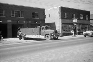 Photograph of a fire truck pulling out of garage onto street at two storey fire hall with anoth…