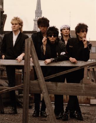 On rooftop, behind wood frames, five young men in black pointy boots, skinny jeans and jackets.…