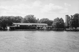 Photograph of water and long boathouse in foreground.