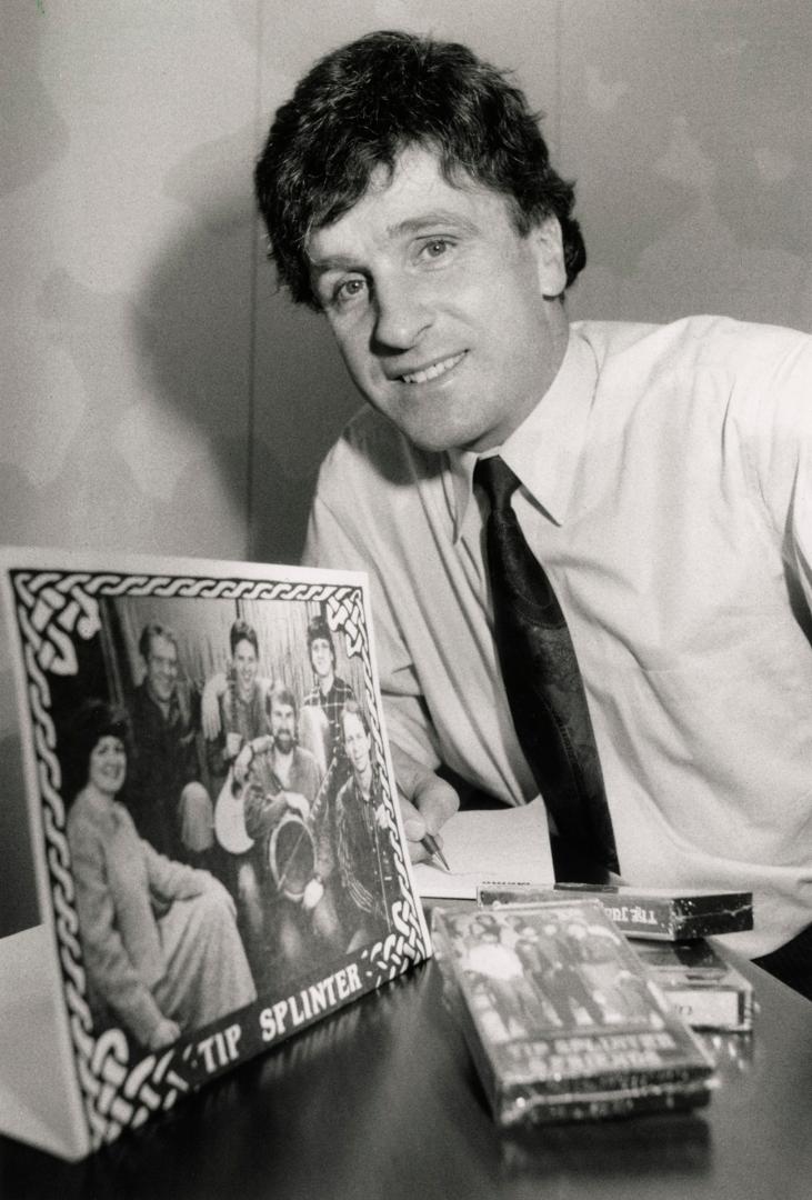 Man in shirt and tie beside album and VHS of Irish group. 