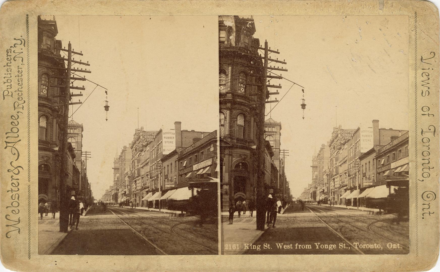 Picture of a street with streetcar tracks showing buildings on both sides, on right stores have…