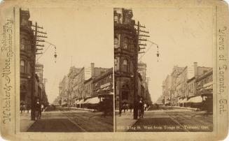 Picture of a street with streetcar tracks showing buildings on both sides, on right stores have…
