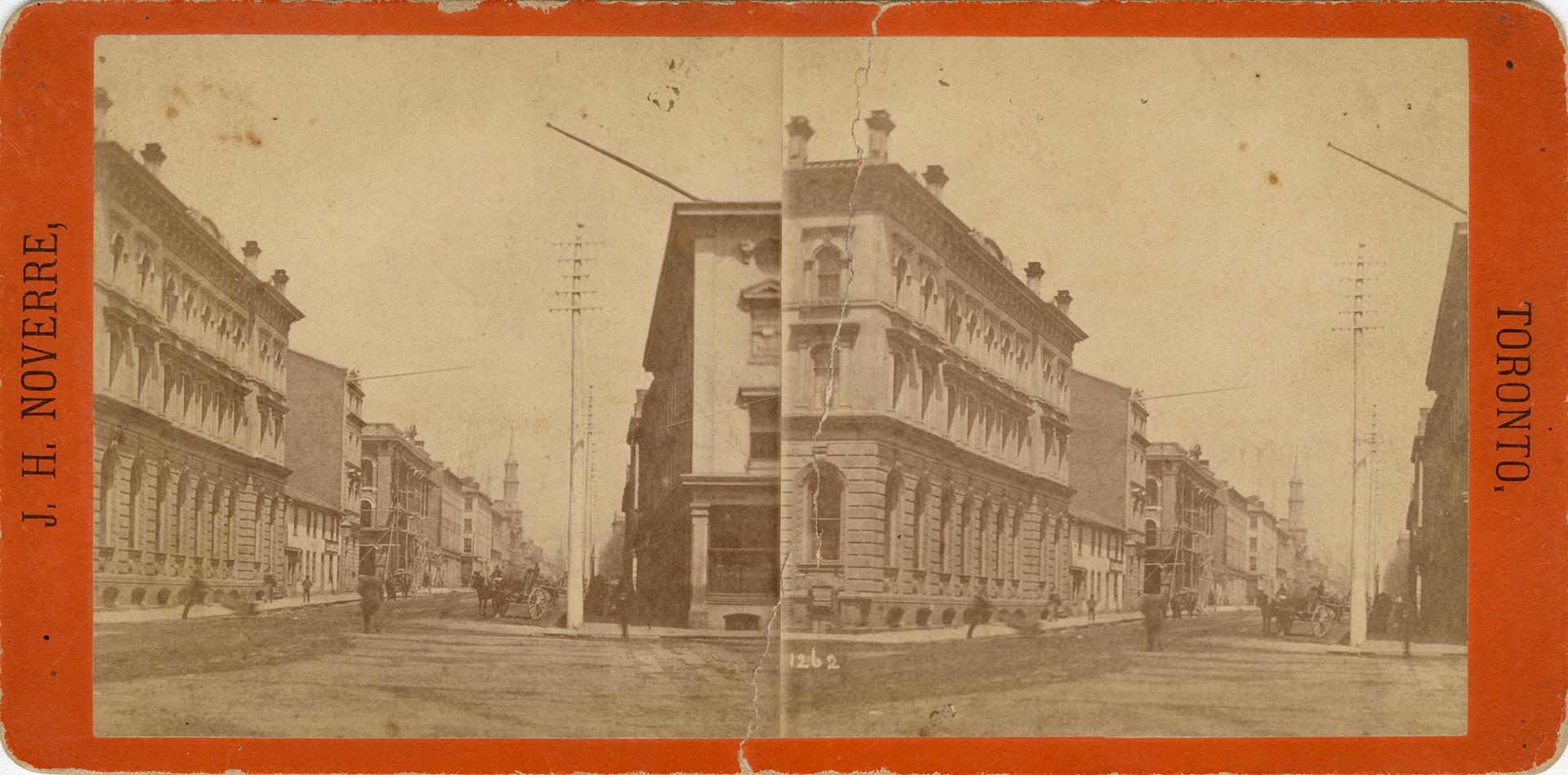Picture of an intersection with buildings on both sides and hydro pole and horse and buggy in d…