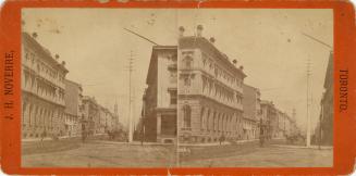 Picture of an intersection with buildings on both sides and hydro pole and horse and buggy in d…