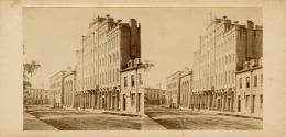 Picture of one side of a dirt street with wooden pavements and buildings including a five store…