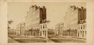 Picture of one side of a dirt street with wooden pavements and buildings including a five store…
