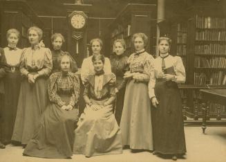 Nine women in long dresses, with long hair tied up.